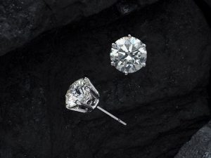 Close-up of luxury diamond earrings on textured black stone, showcasing elegance.